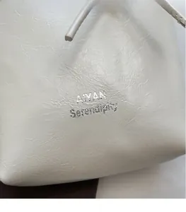 Close-up of white textured leather material and silver logo on minimalist bucket bag