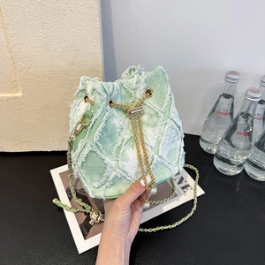 Close-up of light green denim bucket bag featuring raw edge stitching and pearl charms