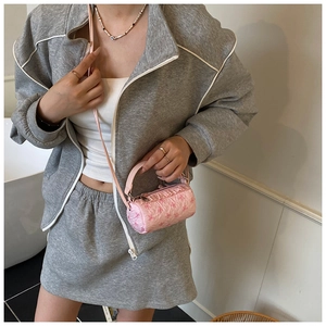 Pink mini cylindrical bag with textured floral design worn on shoulder over grey outfit