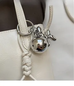Close-up of creative silver balloon dog charm and metallic sphere on a cream leather bag