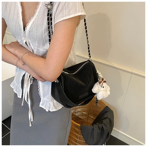 Detail of black textured crossbody bag with silver chain strap and plush puppy charm