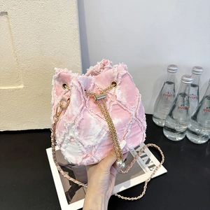 Detail view of pink denim bucket bag featuring frayed edges and pearl chain strap