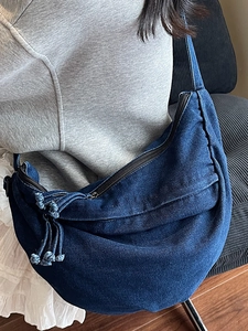 Deep blue denim hobo bag with fringe details, worn by a model in a casual home setting