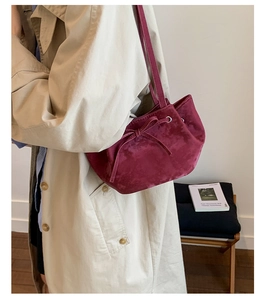 Détail du sac seau en velours bordeaux avec nœud décoratif sur un manteau beige