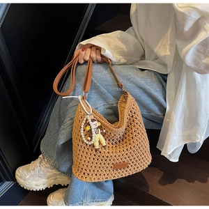 Close-up of woven tote bag with cartoon doll pendant and white pearl chain detail