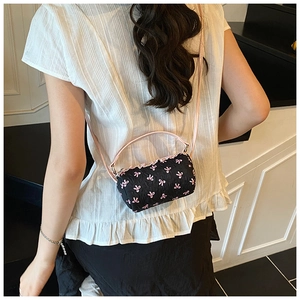 Detail of black cylinder handbag with pink bow embroidery and ruffled top on model