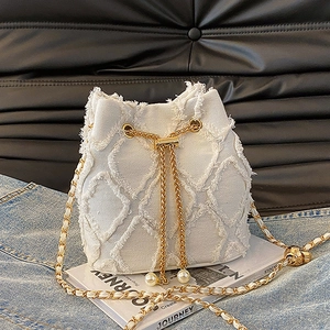 Detail of white denim bucket bag with frayed edges, pearl drawstrings and golden chain