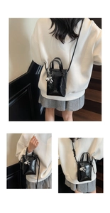 Detail view of mini black glossy leather bucket bag featuring a silver bear charm accessory
