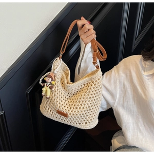 Detail of beige woven crochet tote bag with brown faux leather straps and cute doll pendant
