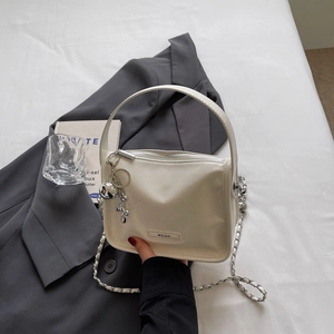 Detailansicht der cremeweißen Mini-Tasche mit Silberkette und kleinem Bären-Anhänger