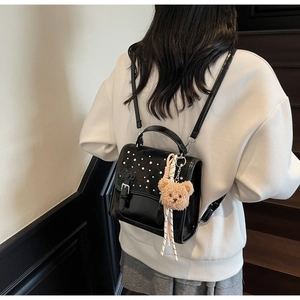 Detail of black patent leather backpack featuring pearls and a cute bear pendant charm