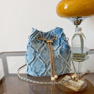 Detailed view of blue denim bucket bag with frayed quilted texture and pearl drawstring