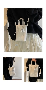 Detail view of mini white bucket bag featuring silver rabbit charm and knotted strap