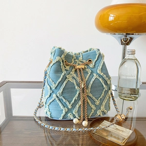 Detail of light blue denim bucket bag with frayed quilted pattern and pearl chain drawstrings