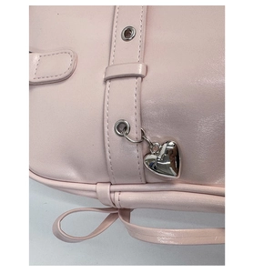 Detail of pink leather bag featuring an adjustable strap and silver metal heart pendant