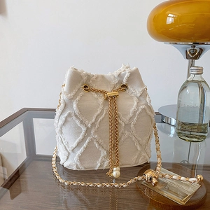 Detail of white tweed bucket bag featuring gold chain strap and pearl drawstring charm