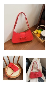 Gros plan détaillé d'un sac baguette tressé rouge avec un nœud en cuir élégant sur bois