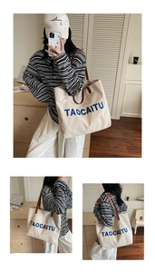 Detailed embroidery of TAOCAITU logo on cream canvas tote with brown leather handles