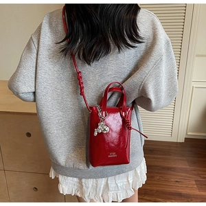 Detail of red glossy mini bucket bag featuring a silver rabbit charm and leather texture