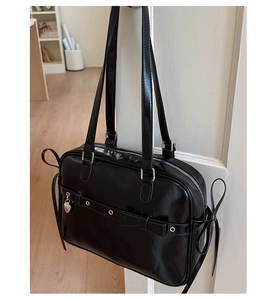 Detail of black glossy handbag with bow decoration and heart pendant on white door