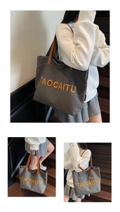 Detail of grey canvas tote with orange TAOCAITU embroidery and brown leather handles