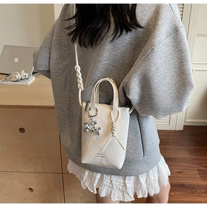 Detail of white mini bucket bag with rope strap and silver dog charm accessory