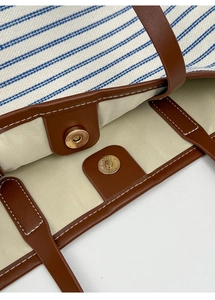 Macro view of the magnetic closure and leather trim on a striped canvas tote bag