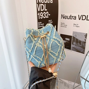 Detail of light blue denim bucket bag with frayed quilted pattern and pearl charm chain