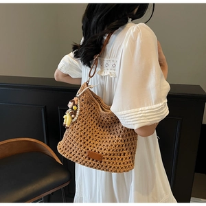 Detail of woven straw tote bag featuring leather shoulder straps and pearl doll charm