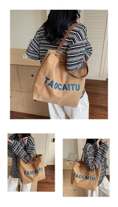 Detail of khaki canvas tote bag with blue letter embroidery and dark brown leather straps