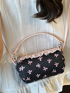 Cylindrical pink bow print shoulder bag with ruffle trim and thin leather strap