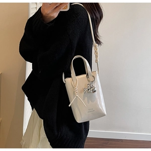 Detail of cream mini bucket bag with woven handle and silver rabbit charm accessory