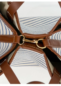 Detail of blue striped canvas tote with brown leather trim and golden metal clasp buckle