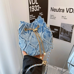Detail of blue denim bucket bag featuring frayed edges, gold chain, and pearl accents