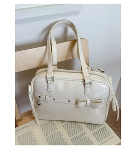 Detail of cream white faux leather Boston bag with bow accent and heart pendant