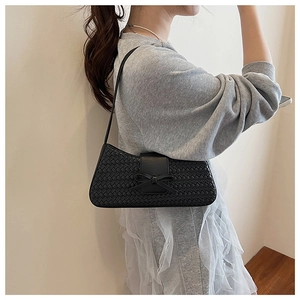 Détail du sac baguette tissé noir avec un nœud et une bandoulière sur un mannequin