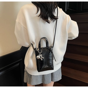 Close-up of black glossy mini bucket bag with silver rabbit charm and logo detail