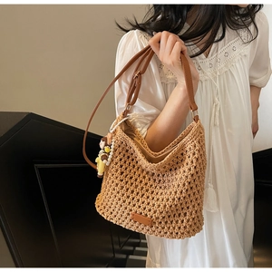 Detail of woven straw tote bag featuring leather straps and a pearl girl charm