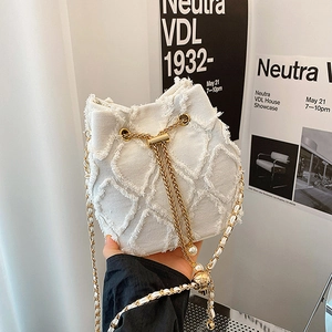 Close-up of white denim bucket bag with frayed edges and pearl chain detail