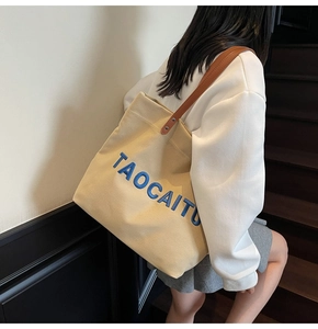 Detail of canvas tote bag featuring blue embroidery and brown leather shoulder straps
