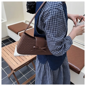 Détail du sac baguette marron tressé avec un nœud décoratif dans un style urbain