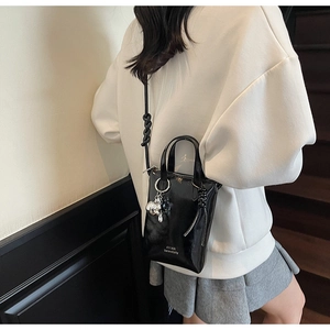 Detail of black patent leather mini bucket bag with silver bear charm and crossbody strap