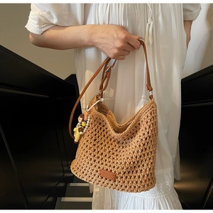 Close-up of woven tote bag with brown adjustable strap and cute cartoon doll charm