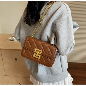 Détail d'un sac bandoulière matelassé marron avec chaîne dorée et fermoir géométrique