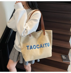 Detail of canvas tote bag with brown leather handles and blue embroidered letters