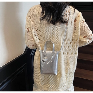 Detailed view of mini silver metallic crossbody bucket bag with bear charm on model