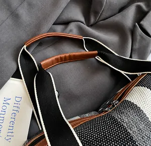 Detalle del bolso tote de cuadros con asa de cuero marrón y correa de hombro tejida