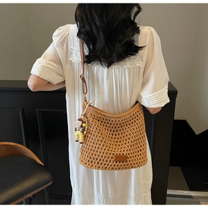 Detail of woven straw tote bag with cute doll pendant and slim leather strap