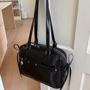 Close-up of black smooth leather JK style shoulder bag with silver eyelets and bow detail