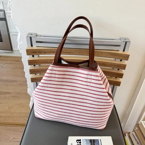 Large red and white striped canvas tote bag with brown leather handles on wooden chair